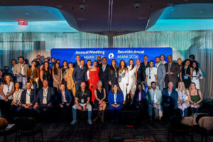Large group of professionals posing on a stage in front of a blue 'Annual Meeting MIAMI 2026' banner.